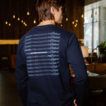 A man wearing a navy blue long-sleeve shirt with a white graphic print on the back, photographed from behind in a dimly lit indoor environment.