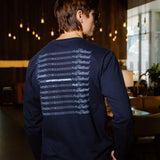 A man wearing a navy blue long-sleeve shirt with a white graphic print on the back, photographed from behind in a dimly lit indoor environment.