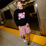A man walking off a train at a station, wearing a black crewneck sweatshirt with a pink and white graphic print, pink and white striped shorts, black and yellow socks, and white sneakers.