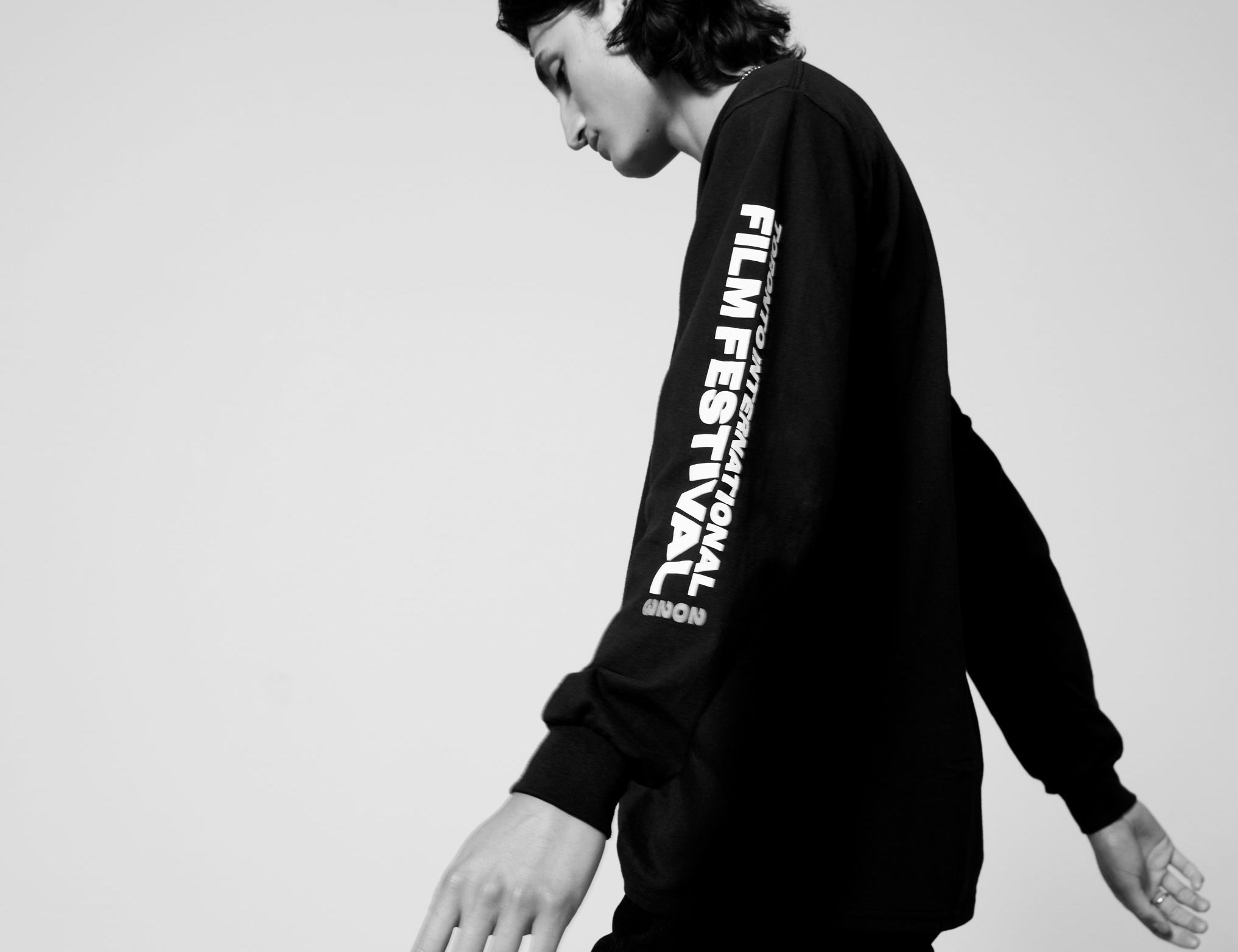 Black and white photo of a male model walking while wearing a black TIFF 2023 sweatshirt