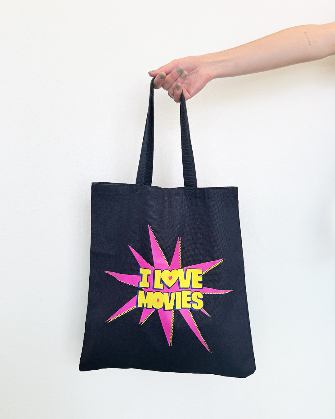 Navy tote bag with 'I love movies' design held by a hand on a white background