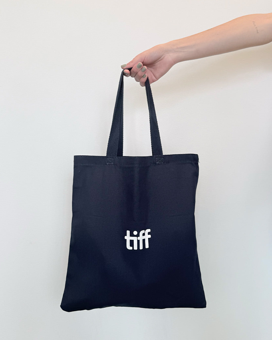 Navy tote bag with 'tiff' logo held by a hand against a white background