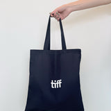 Navy tote bag with 'tiff' logo held by a hand against a white background