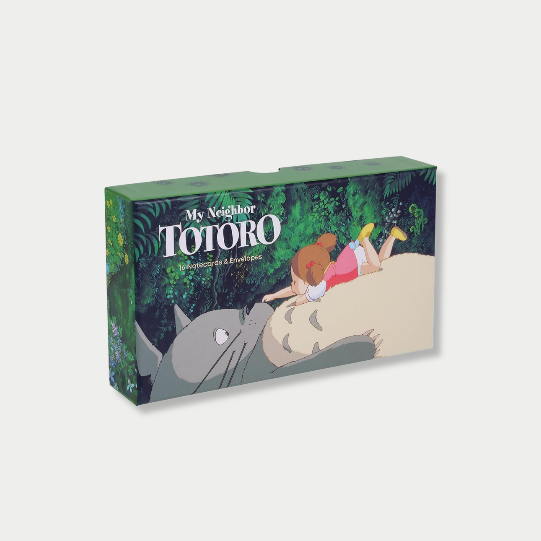 An angled studio shot of a green "My Neighbor Totoro: 16 Notecards & Envelopes" stationery box featuring Mei lying on Totoro's stomach.