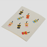 A square cream-colored dishcloth with a waffle texture, printed with a pattern of colorful iced coffee cups, on a light gray background.