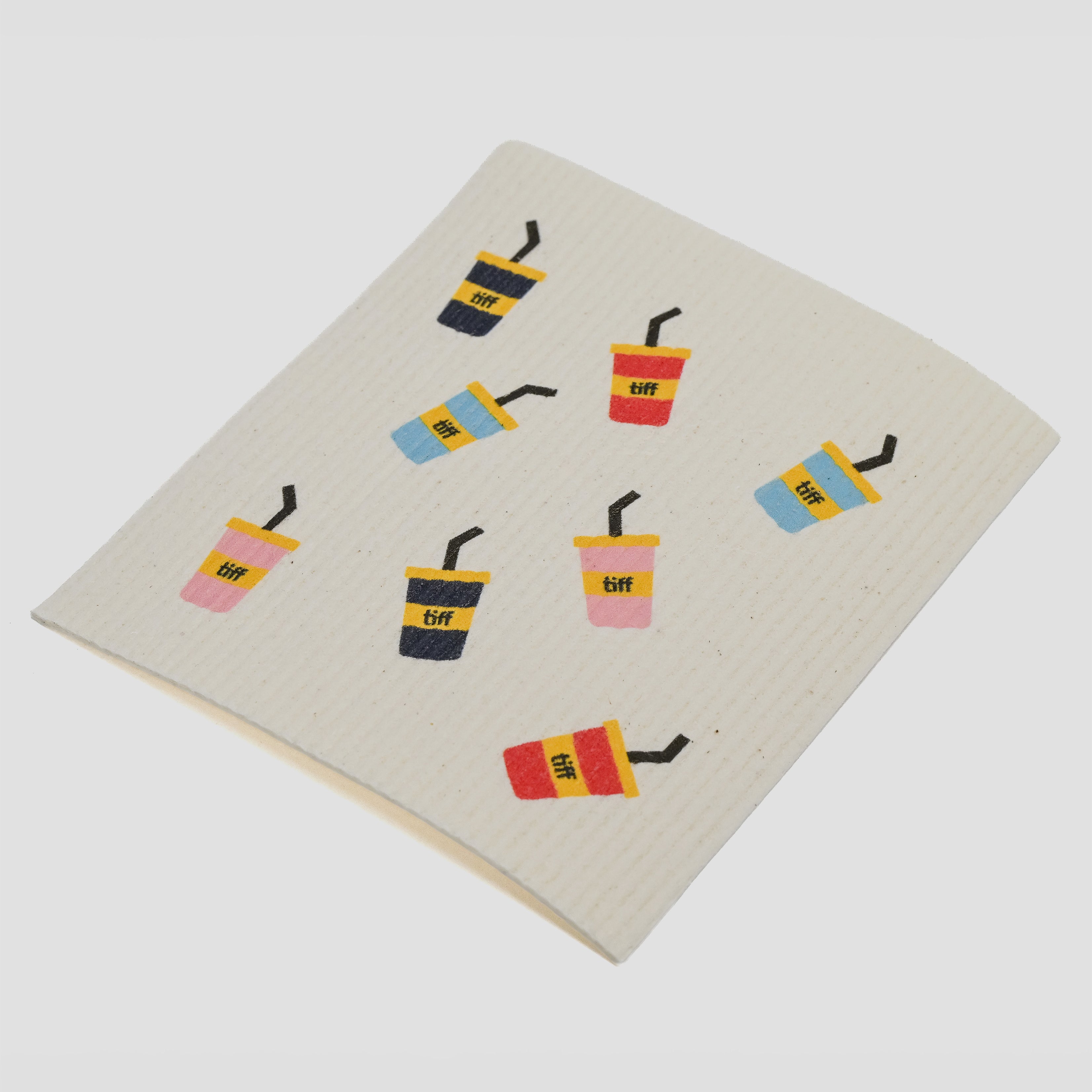 A square cream-colored dishcloth with a waffle texture, printed with a pattern of colorful iced coffee cups, on a light gray background.