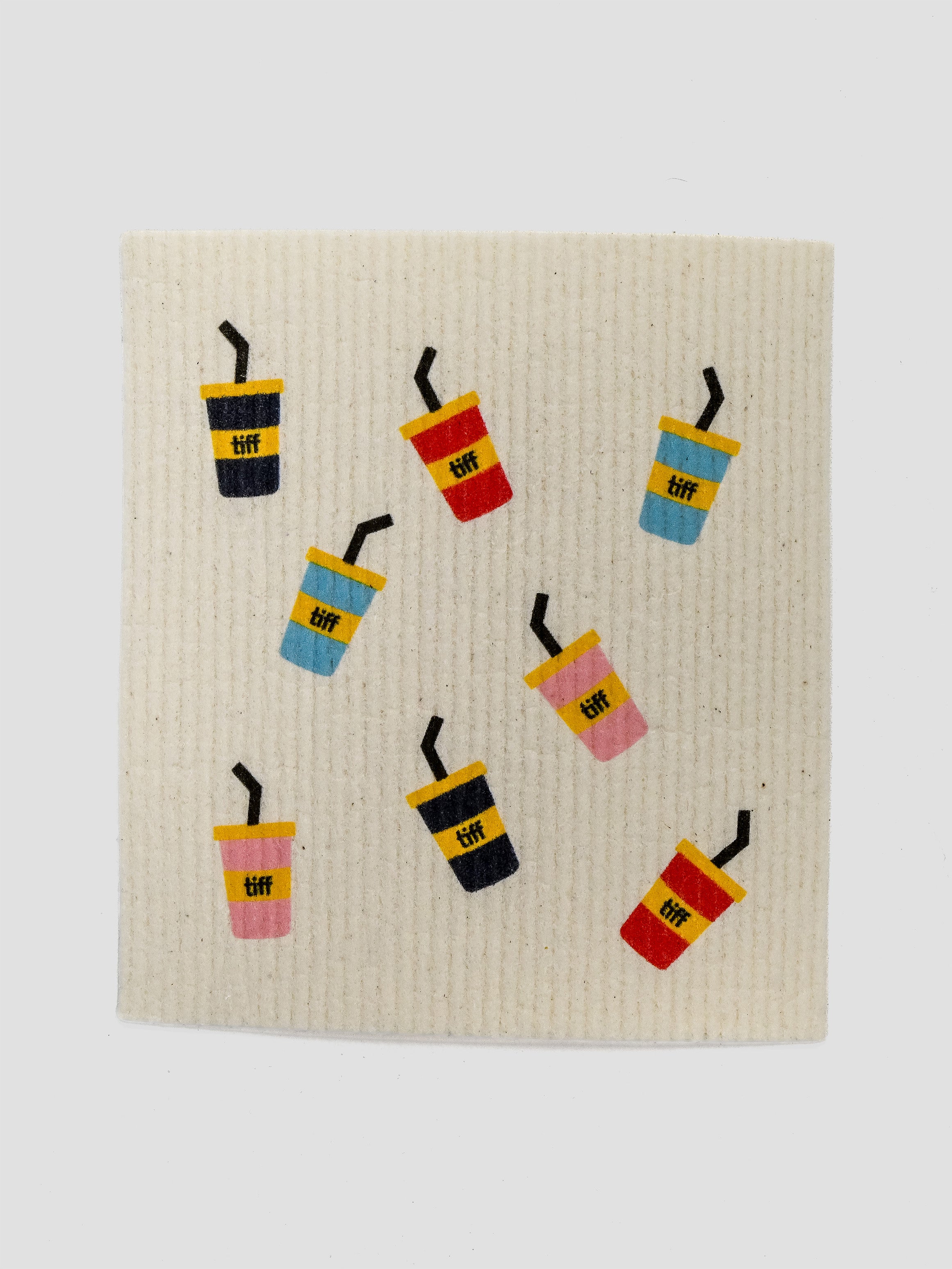 A square cream-colored textured fabric napkin featuring a playful pattern of colorful iced coffee cups with the word 'TIFF' printed on them, set against a plain light gray background.