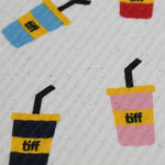 A close-up of a textured white fabric featuring a repeating pattern of colorful drink cups with yellow bands and the text 'tiff' printed in black.