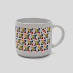 A white ceramic coffee mug featuring a colorful geometric pattern of repeating 3D cube-like shapes in red, yellow, blue, and green, with a small red logo on the upper right side, set against a solid light gray background.