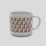 A white ceramic coffee mug featuring a colorful geometric pattern of repeating 3D cube-like shapes in red, yellow, blue, and green, with a small red logo on the upper right side, set against a solid light gray background.