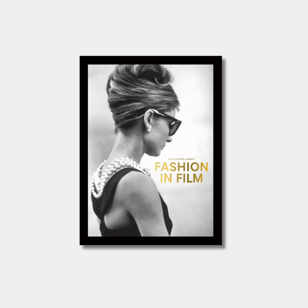 A black and white profile of Audrey Hepburn as Holly Golightly in Breakfast at Tiffany's, wearing a beehive hairstyle, oversized sunglasses, and pearls, serves as the cover for the book "Fashion in Film" by Christopher Laverty.
