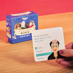 A hand holds a trivia card about artist Frida Kahlo next to the box for the Ridley's Inspirational Women Trivia Game.
