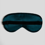 A dark teal satin sleep mask with a black elastic strap, laid flat against a light gray background.