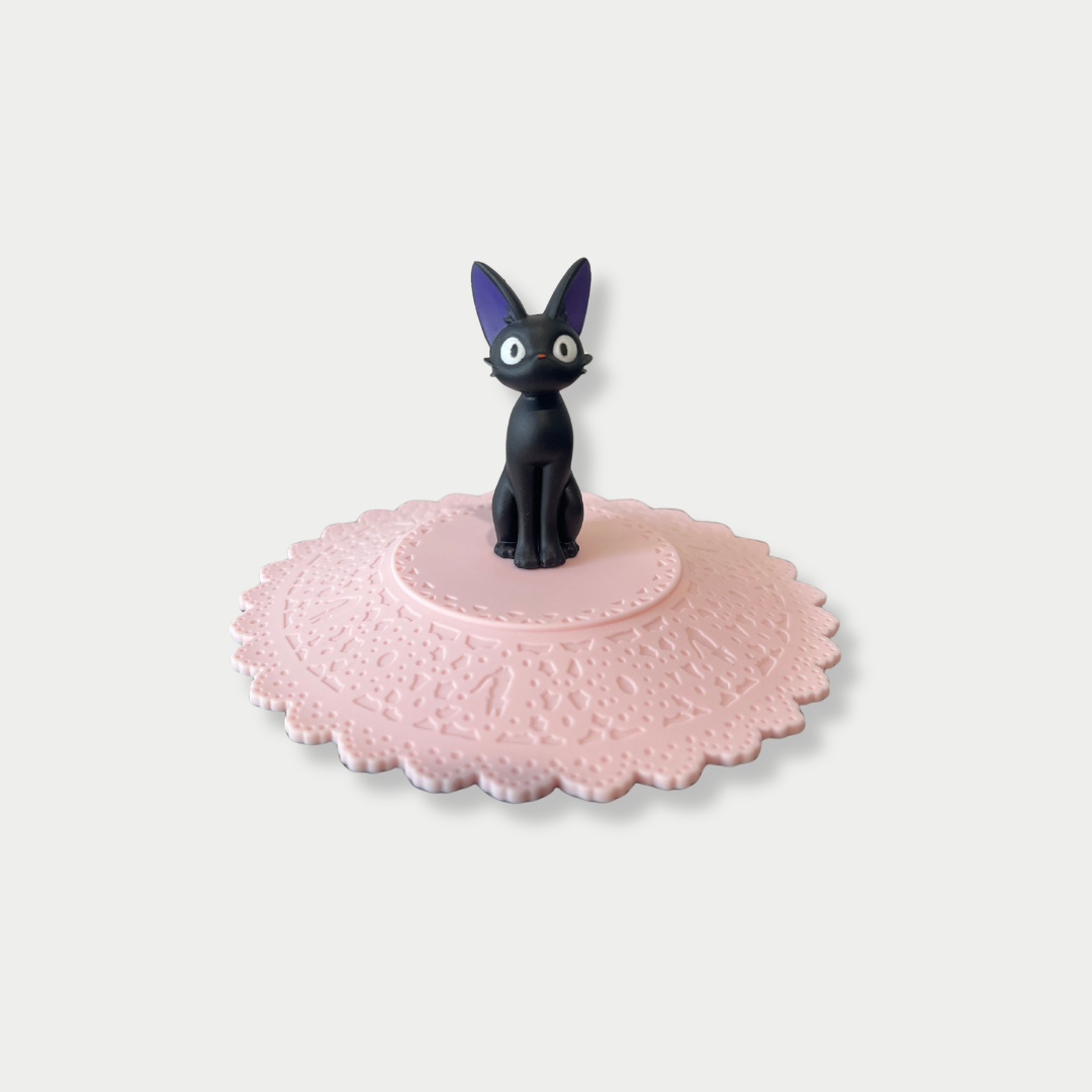 A black Jiji figurine stands in the center of a scalloped pink silicone mug lid.