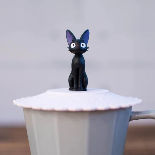 A close-up shot focuses on a small Jiji figurine sitting atop a pink scalloped silicone lid on a grey mug.