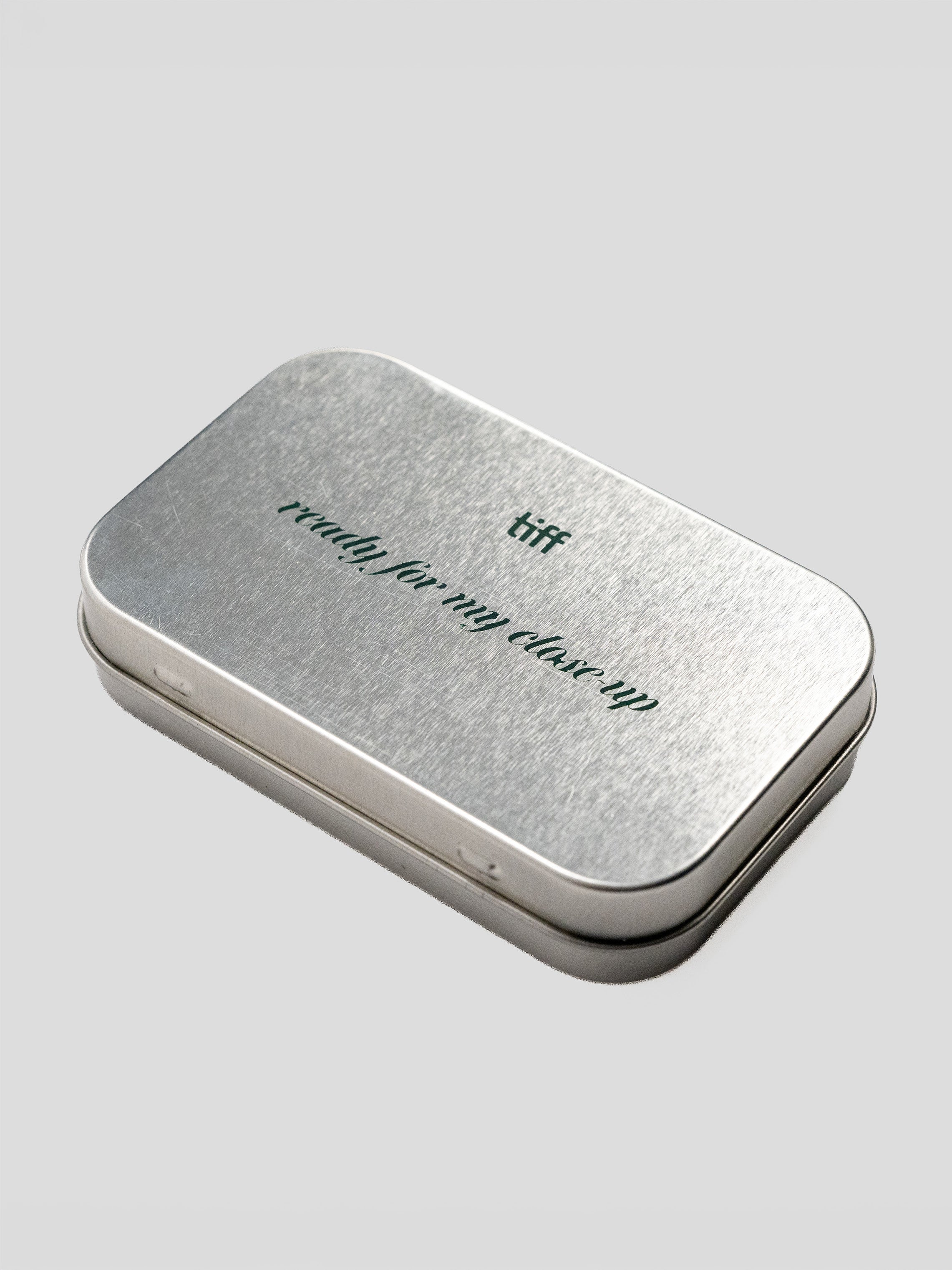 A rectangular silver metal tin with rounded corners, featuring the words 'ready for my close-up' and 'tiff' printed on the lid, set against a solid light gray background.