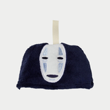 A close-up shot shows a small, dark blue plush pouch with an embroidered No-Face mask and a fabric hanging loop.