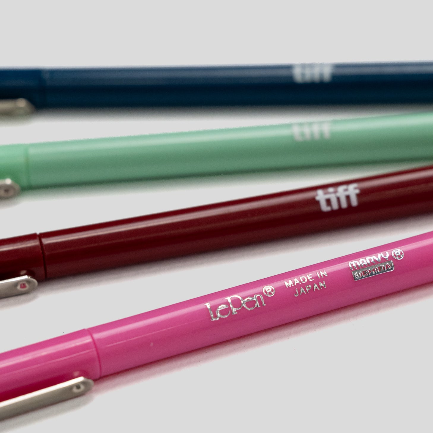 Four LePon tiff mechanical pencils in navy blue, mint green, burgundy, and pink, arranged diagonally on a light gray background.