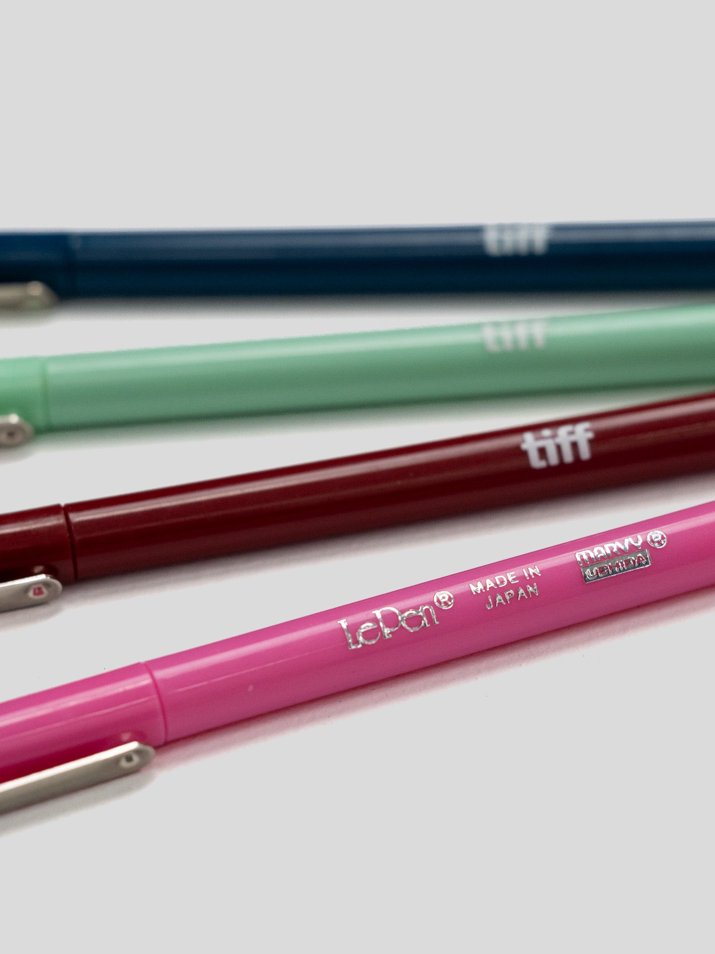 Four LePon tiff mechanical pencils in navy blue, mint green, burgundy, and pink, arranged diagonally on a light gray background.