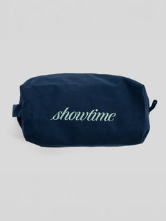 A navy blue canvas cosmetic pouch with the word 'showtime' embroidered in light green script across the front, set against a plain light gray background.