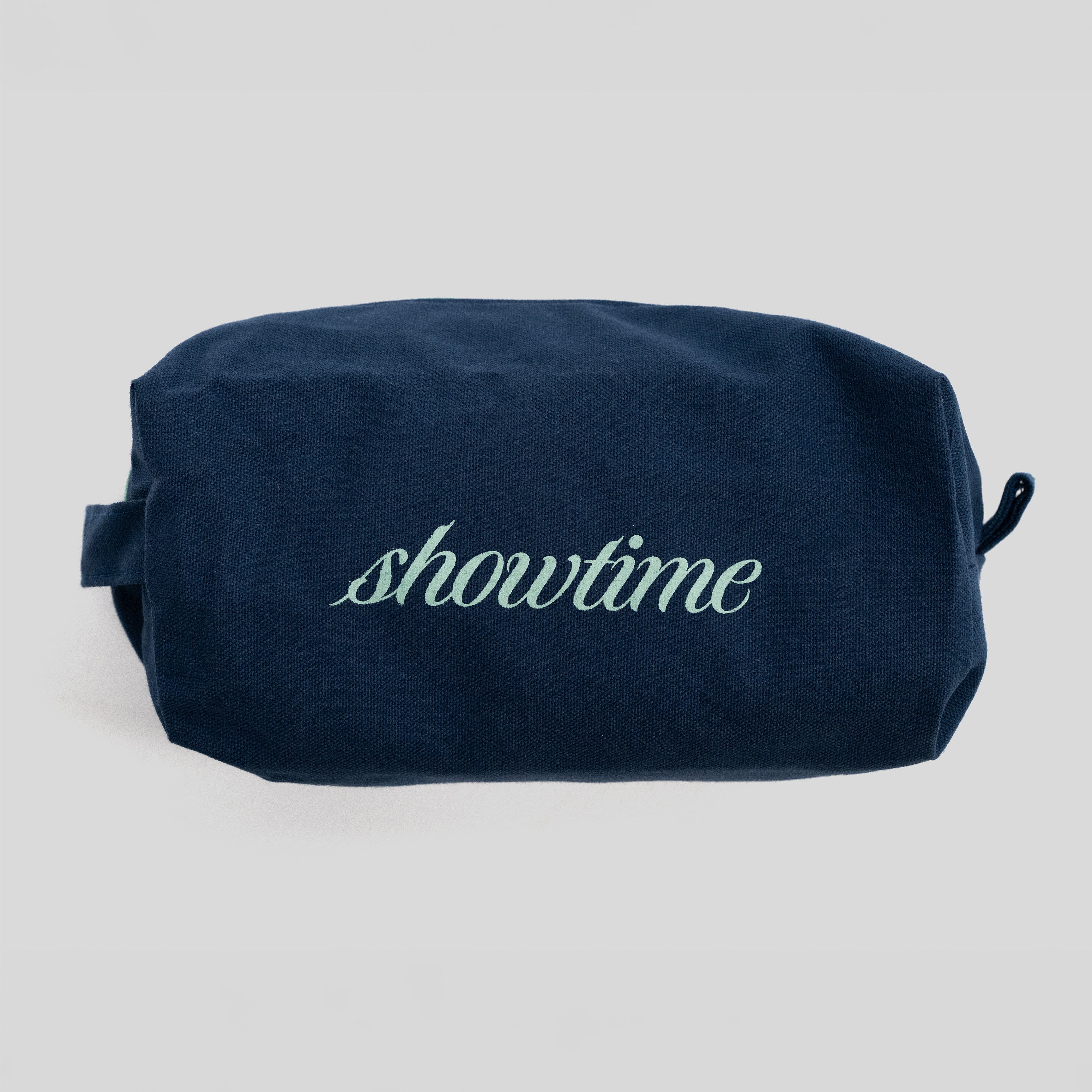 A navy blue canvas cosmetic pouch with the word 'showtime' embroidered in light green script across the front, set against a plain light gray background.