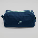 A navy blue canvas toiletry bag with a mint green zipper and a mint green 'tiff' logo on the front, photographed on a neutral light gray background.