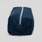 A navy blue canvas pouch with a mint green zipper, photographed on a neutral light gray background.