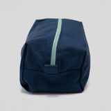 A navy blue canvas pouch with a mint green zipper, photographed on a neutral light gray background.
