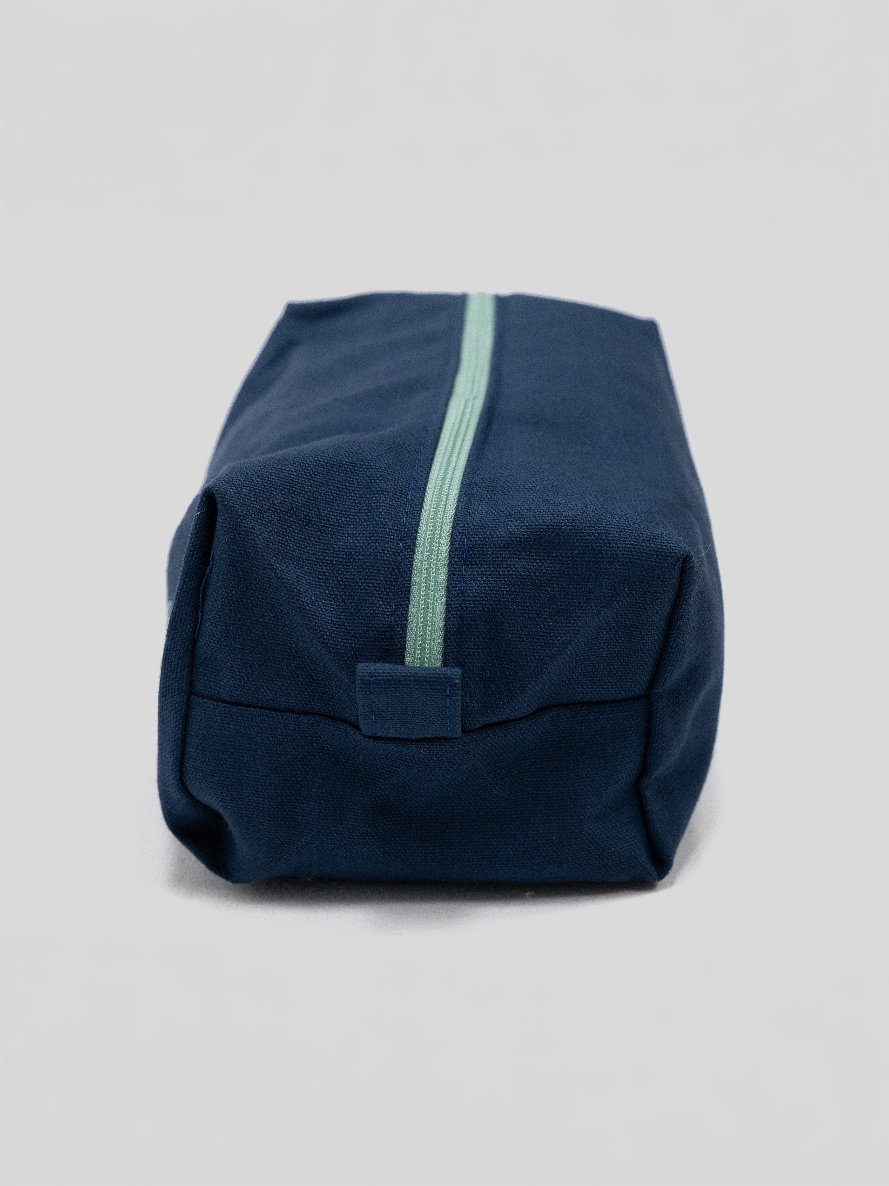 A navy blue canvas pouch with a mint green zipper, photographed on a neutral light gray background.