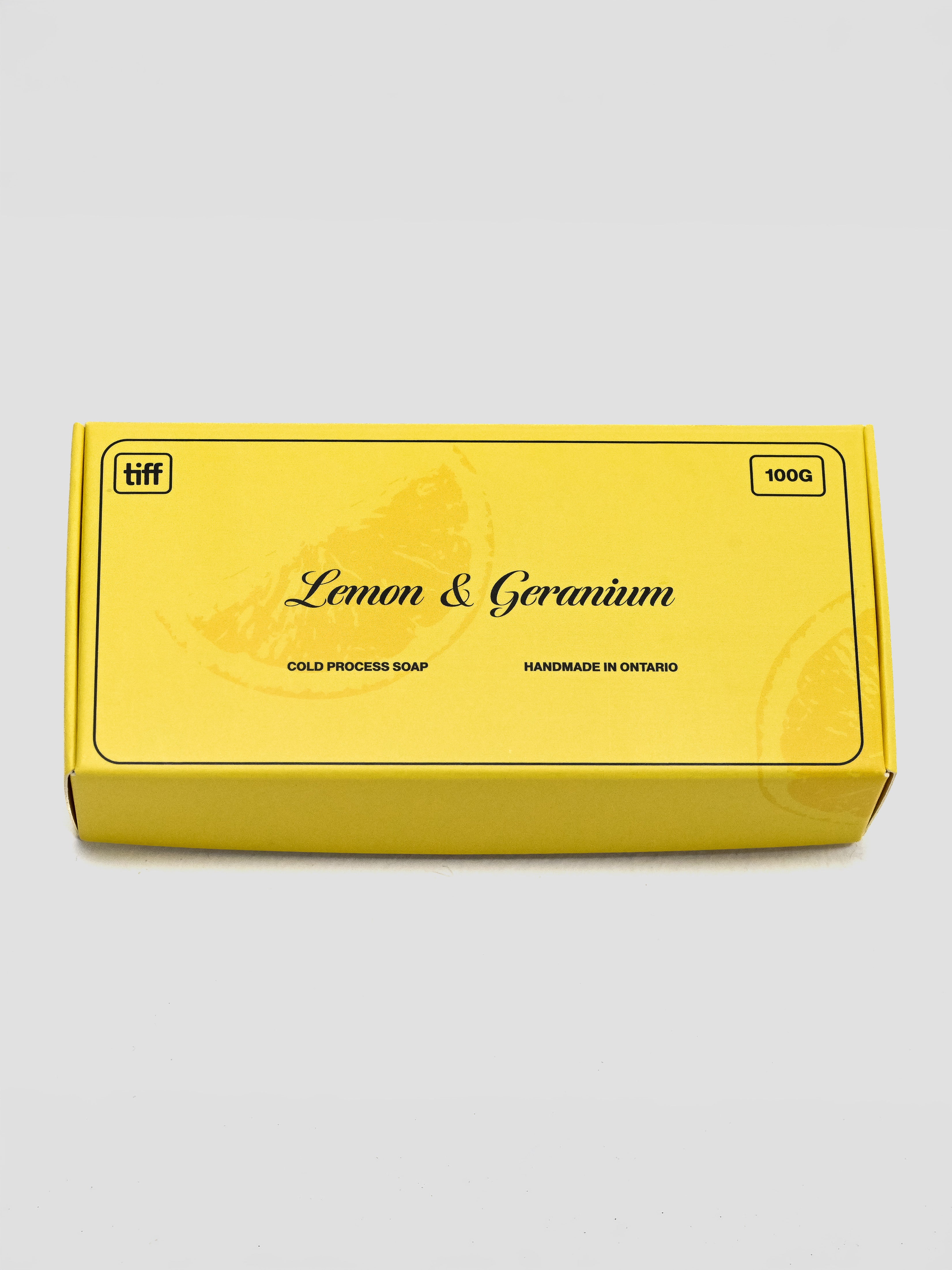 A yellow rectangular box of TIFF Lemon & Geranium cold process soap, 100g, shown on a light gray background.