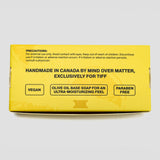 A bright yellow product box for Mind Over Matter Vegan Olive Oil Base Soap, featuring black text and product details, photographed on a light gray background.