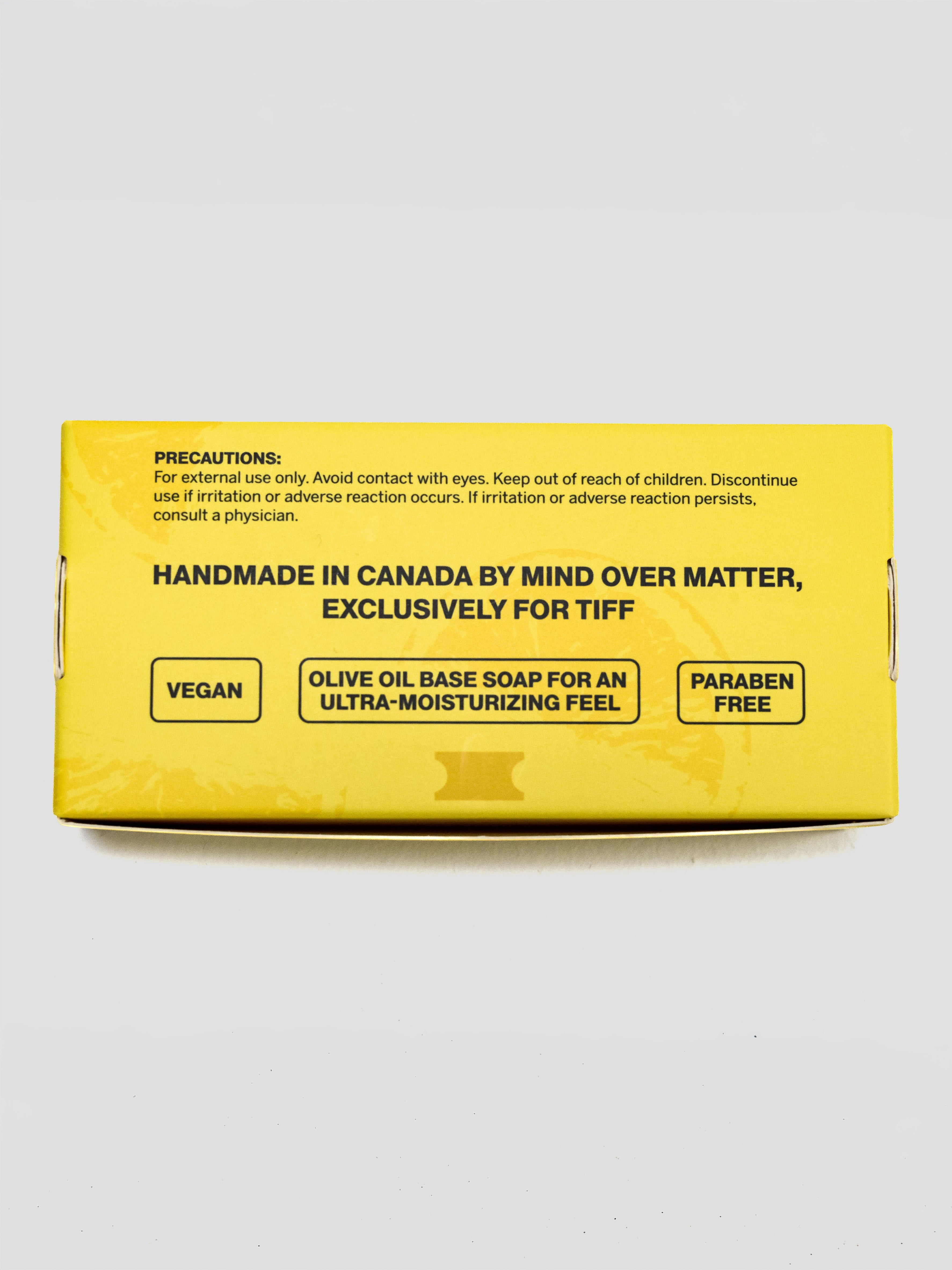 A bright yellow product box for Mind Over Matter Vegan Olive Oil Base Soap, featuring black text and product details, photographed on a light gray background.