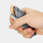 A hand squeezes a grey rubber shark toy, causing a small, tan-colored human leg to pop out from its open mouth.