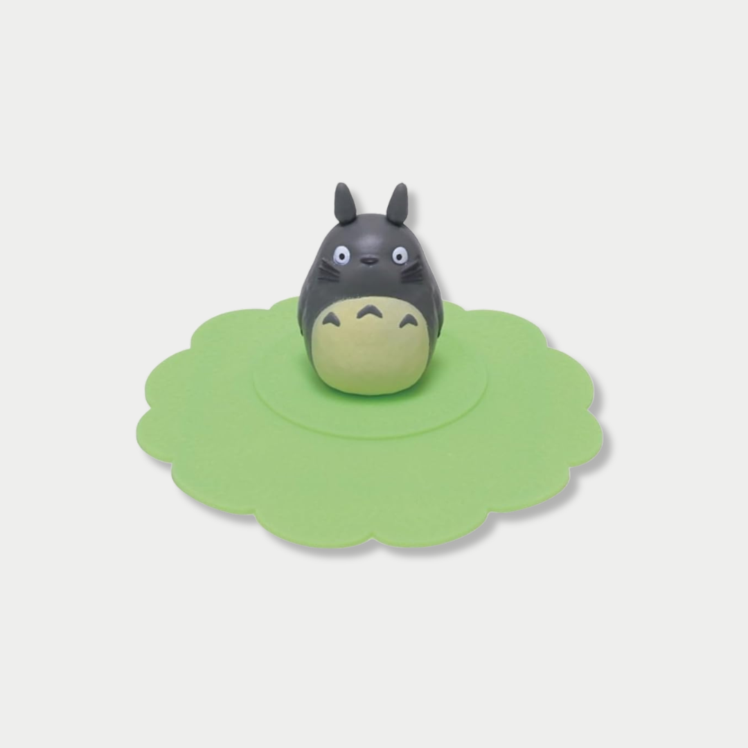 A grey Totoro figurine stands in the center of a scalloped green silicone mug lid.