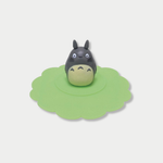 A grey Totoro figurine stands in the center of a scalloped green silicone mug lid.