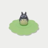 A grey Totoro figurine stands in the center of a scalloped green silicone mug lid.