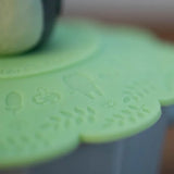 A close-up shot displays debossed Studio Ghibli icons like acorns, mushrooms, and soot sprites on a green silicone lid.