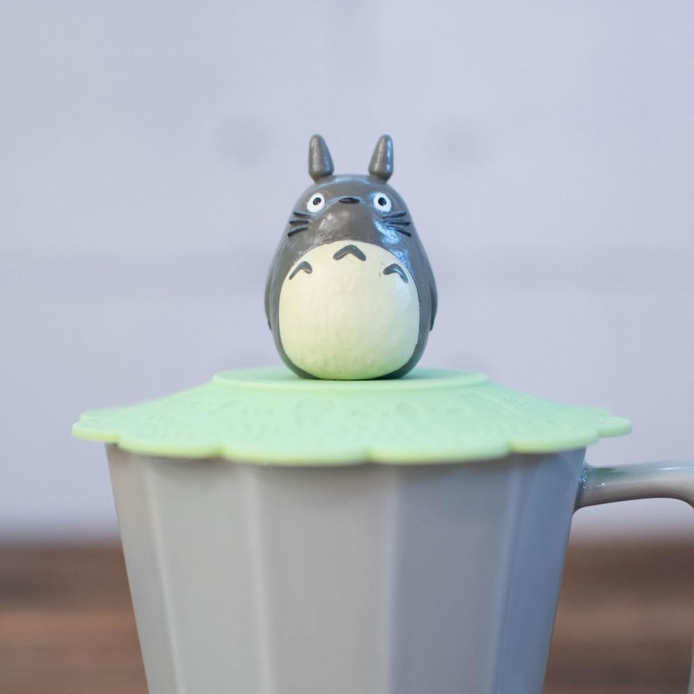 A close-up shot focuses on a small grey Totoro figurine sitting atop a green scalloped silicone lid on a grey mug.