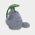 A fluffy gray Totoro plush toy holds a large green leaf overhead like an umbrella.
