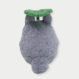 Back view of fluffy gray Totoro plush toy holding a large green leaf overhead like an umbrella.



