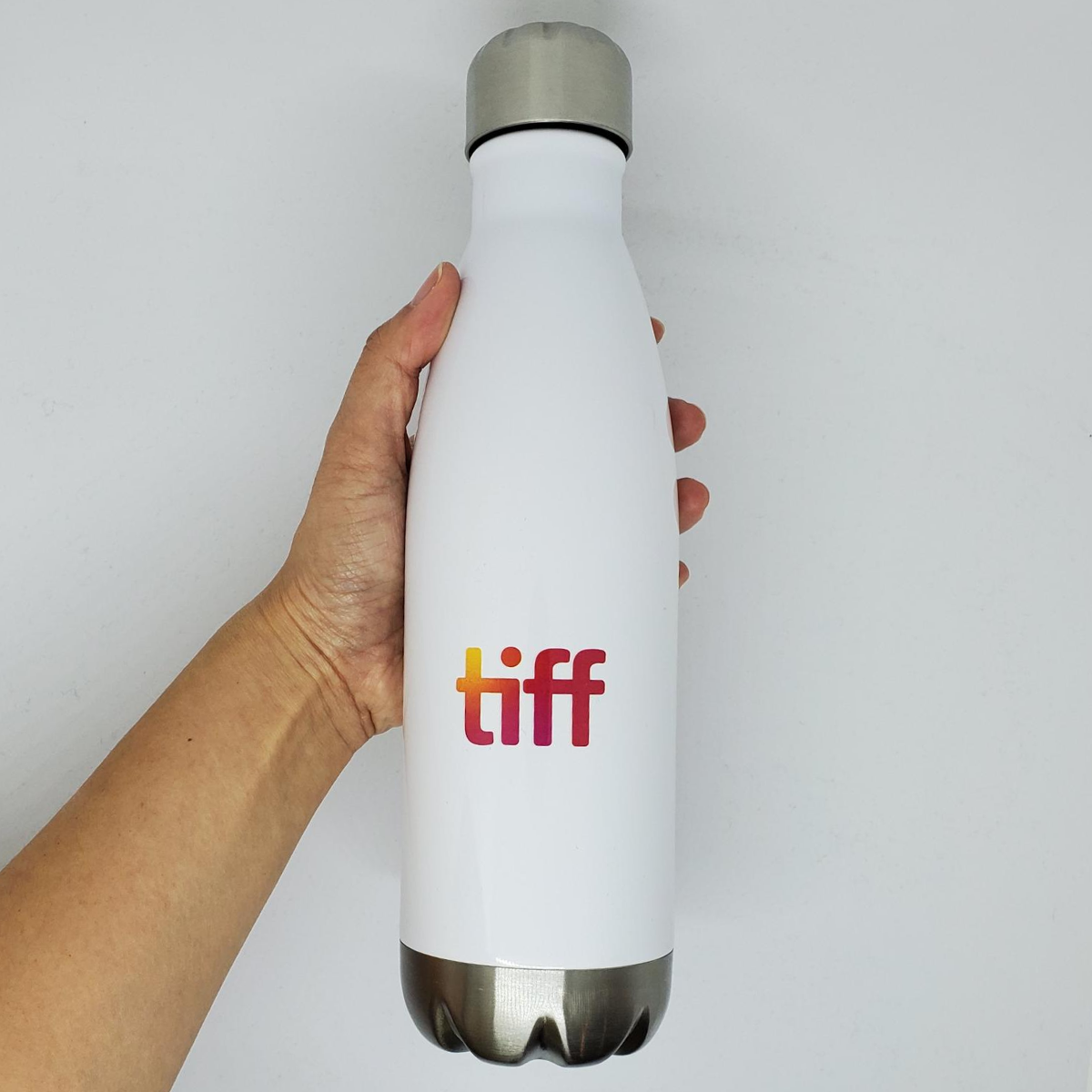Hand holding white water bottle reverse side with TIFF logo in an orange gradient.
