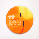 Flat orange circle magnet. Image is of two separate silhouettes of people gazing at a glowing structure, which represents the TIFF Bell Lightbox. "TIFF Toronto International Film Festival, September 6-16, 2018" in white lettering.