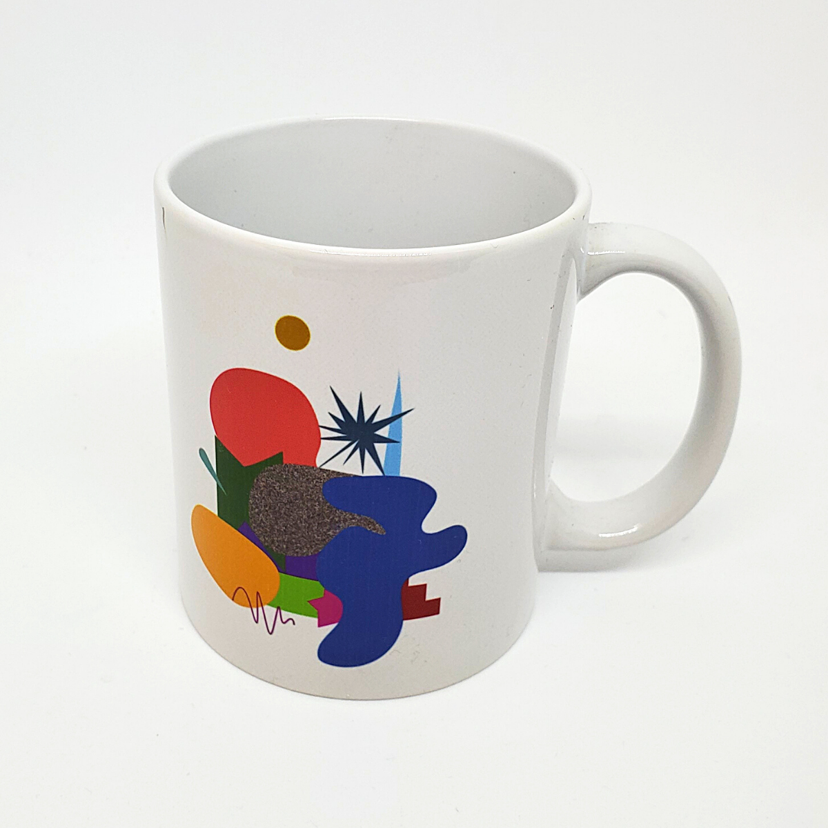 White mug with a variety of abstract shapes and lines in different colours. The design for the 2019 Festival logo.